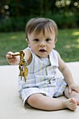 Baby boy sitting on blanket in garden holding set of keys