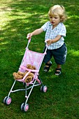 Blonde baby boy with toy pushchair in garden