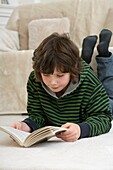 Boy lying on living room floor reading a book