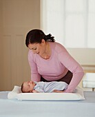 Woman gently lowering baby boy onto changing mat