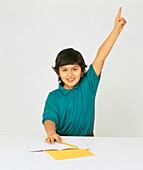 Boy sat at desk with one arm in the air