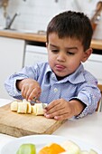 Boy using knife to slice banana, tongue sticking out