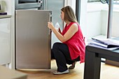 Woman opening fridge door with baby bottle in the other hand