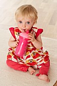 Baby girl holding plastic bottle and drinking from a straw