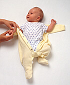 Woman putting babygro on smiling baby boy lying on back