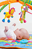 Baby lying on back and looking up at toys hanging from frame