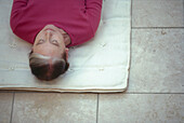 Woman with eyes closed lying on back on thin white mattress