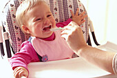 Baby being fed in a high chair, smiling, laughing