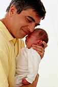 Man holding a baby close to his face, supporting its head