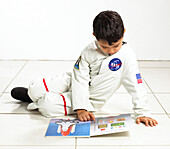 Boy in space suit sitting on floor and reading book