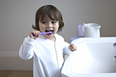 Girl in pyjamas brushing teeth standing at sink in bathroom