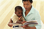 Boy sitting on woman's lap holding book