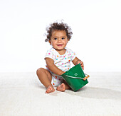 Baby girl sitting on floor holding green bucket