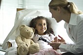 Doctor holding otoscope over girl in bed