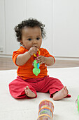 Baby girl sitting on rug playing with plastic toy