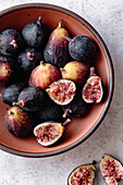 Fresh figs in a terra cotta bowl on a marble work surface