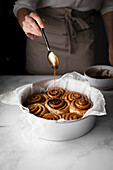 A baker drizziling glaze on cinnamon buns