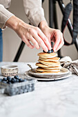 Frauenhände arrangieren Pancakes mit Blaubeeren