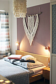 Double bed below sconce lamps and macramé wall-hanging in bedroom