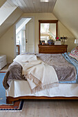 Doppelbett, Holzkommode, ddarüber Wandspiegel im Schlafzimmer mit Dachschräge