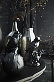 Still life with black decorative birds, silver vases and dried flowers