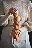 A woman is holding baked baguettes in an apron