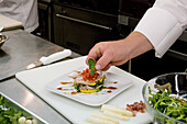 Chef's hand adding garnish to a plate in a restaurant kitchen