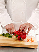 Chef's hands with a knife cutting a red bell pepper