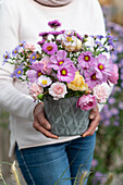 Frau hält Vase mit Spätsommer-Strauß aus Schmuckkörbchen, Rosen, Herbstastern und Herbstanemone