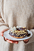 Woman holds in her hands a plate with a donut covered with chocolate