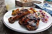 A grilled BBQ chicken leg and thigh with cole slaw and poasted potatoes on a stoneware plate in a casual picnic setting