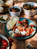 Ready dish of mozzarella and tomatoes, with bread, olives and anchovies