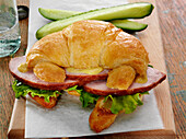 Baked ham sandwich with lettuce and Dijon mustard on a croissant with pickle spears