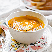 Orange pumpkin soup with a cream and pepper in white stoneware bowl
