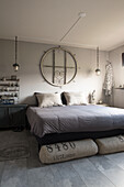 Double bed with linen scatter cushions below round window frame on wall