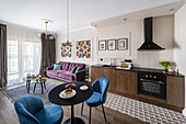 Dining area with blue upholstered chairs in front of small kitchenette and purple sofa in open plan living area