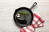 Black cast iron frying pan with oil, garlic, pepper and rosemary