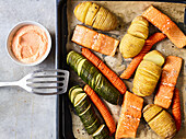 Hasselback vegetables with salmon fillets on a baking tray