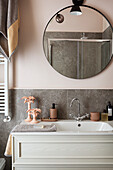Weißer Waschtisch und Spiegel im Bad mit rosa Wänden und grauen Fliesen