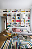 Floor-to-ceiling bookcase and sofa in living room with books on coffee table and side table