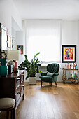 Seating area with green armchair and houseplant next to window with wooden cabinet in foreground