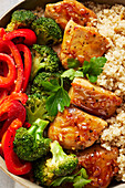 A quinoa bowl with glazed chicken, broccoli and peppers (close up)