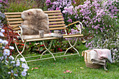 Gartenbank mit Sitzfell am Herbstbeet mit Astern und Bergenien, Korb mit Decke