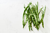 Romano flat green beans on white marble table top view