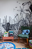 Bücherständer und Polsterstuhl vor Tapete mit Dschungelmotiv im Kinderzimmer