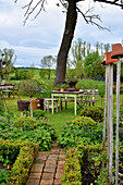 Bauerngarten mit Buchshecken und Storchschnabel im Frühling, Tisch und Bank mit Töpfen auf dem Rasen