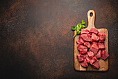 Raw beef meat chopped in cubes with bunch of fresh parsley on wooden cutting board