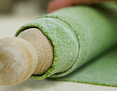 Green pasta dough around a wooden rolling pin