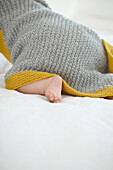 Baby girl crawling off with knitted hooded blanket on back