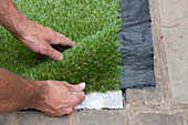 Man placing sheet of artificial turf at edge of path
